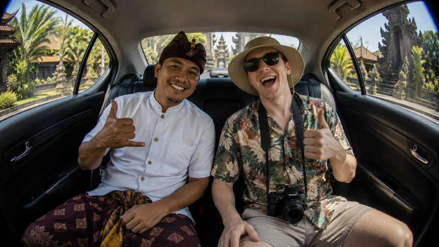 A Booma driver and a traveller in the back seat, both smiling, outside a Balinese temple